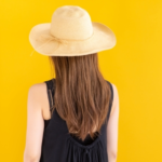 麦わら帽子をかぶったロングヘアの女性の後姿　マスタードカラーの背景