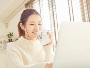 パソコンを見ながらコーヒーを飲む笑顔の女性