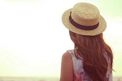 海岸で海を眺める麦わら帽子をかぶった女性