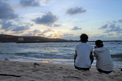 砂浜に座って朝日を見るカップル